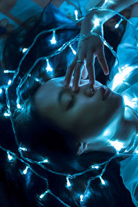 High angle view of woman with illuminated string lights lying on bed