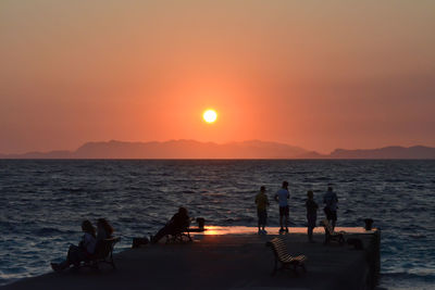 Silhouette people on beach against sky during sunset