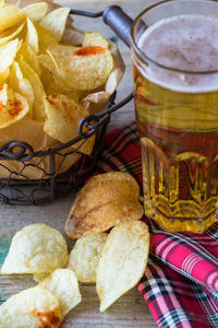 High angle view of fresh potato chips in metal basket by beers on table