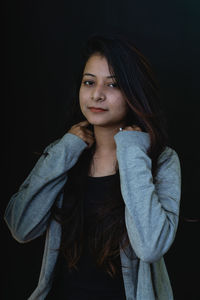 Portrait of young woman standing against black background