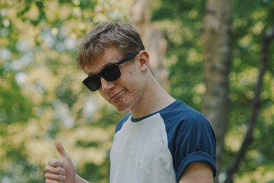 Portrait of young man wearing sunglasses standing against trees