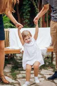 Little blonde girl playing jumping and holding her young parents hand in the garden. 