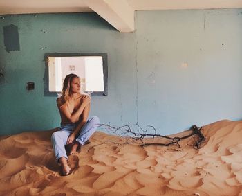 Full length of woman sitting on sand in abandoned room