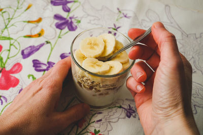 Close-up of a woman's hands holding a glass of yogurt with jam, oat flakes and banana