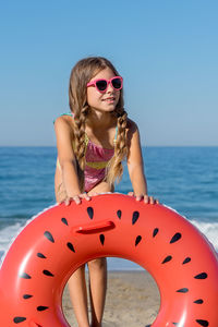 A girl in a swimsuit plays with an inflatable ring on the beach. vertical shot.