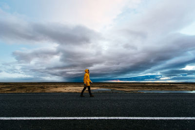 Side view of man walking on roadside against sky