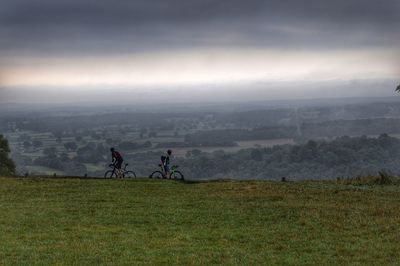 People riding bicycle on field against sky