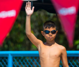 Portrait of shirtless boy with hand raised in sunny day