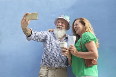 Mature couple taking selfie while standing against blue background