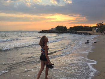 Woman standing on beach against sky during sunset