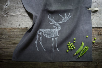 High angle view of animal drawing on black fabric by green peas