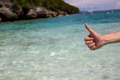 Close-up of hand showing thumbs up against sea