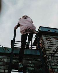 Low angle view of man climbing on building against sky