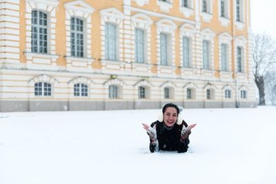 Portrait of smiling woman lying on snowy road against building