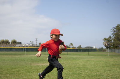 Young boy holding his glove and running across the tball field