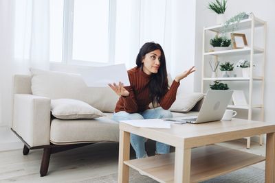 Young woman using digital tablet while sitting on sofa at home