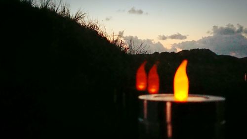 Close-up of lit candle against sky during sunset