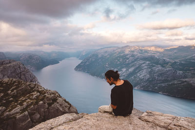 Man sitting on rock looking at mountains against sky