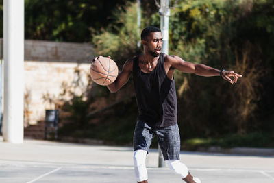 Determined african american male athlete playing basketball on court in summer and looking away