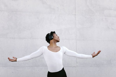 Young male dancer with arms outstretched doing rehearsal against white wall