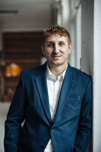 Smiling businessman leaning on wall at office