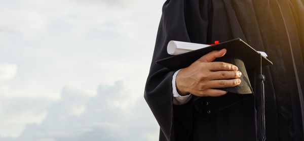 Midsection of man holding cigarette against sky