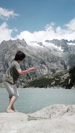 Boy standing on rock by lake against mountains