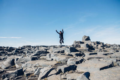 Wide angle of woman jumping  on rock against sky