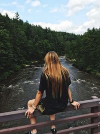 Rear view of woman sitting on railing over stream