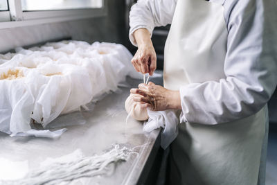 Skilled chef wrapping cheese in cloth at factory