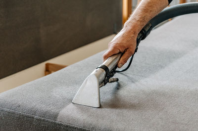 Close-up image of professional cleaning service doing a deep clean of sofa in living room.