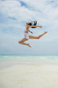 Young woman jumping over sea against sky