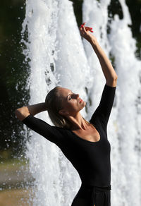 Beautiful woman with hand raised standing against fountain