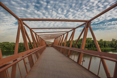 Footbridge over river against cloudy sky during sunset