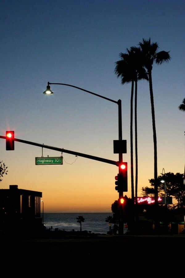 sunset, silhouette, clear sky, palm tree, tree, street light, transportation, sea, built structure, building exterior, street, mode of transport, sky, architecture, sun, outdoors, lighting equipment, men, dusk