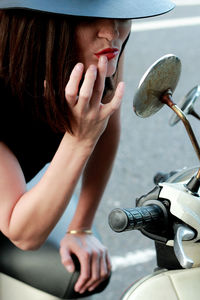 Woman touching lips while looking in side-view mirror of motor scooter