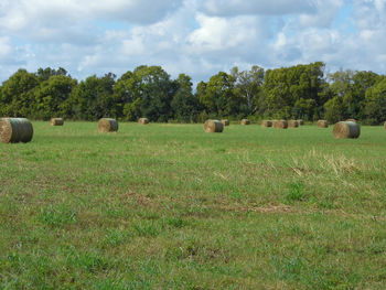 Hay bales on field against cloudy sky