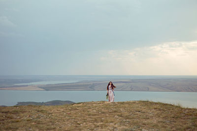 Woman stands on a mountain cliff in a blue long dress in summer
