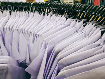 Various sizes of white uniform shirts with hangers on curved rack with selective focus