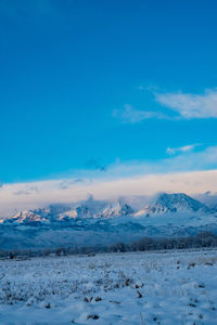 Snow covered landscape against blue sky