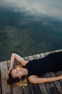 Woman lying down on pier by river against sky