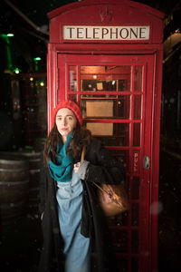 Portrait of woman standing against telephone booth