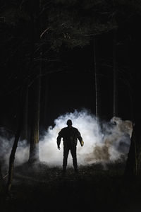 Silhouette demon standing in front of smoke in forest at night