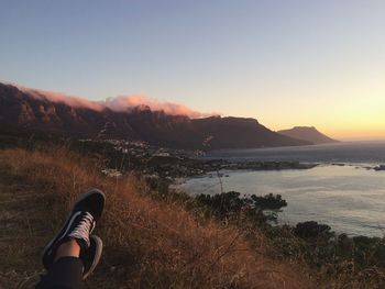 Low section of woman resting on mountain by sea during sunset