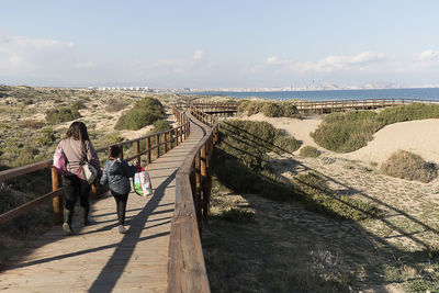 Rear view of mother and daughter walking on footbridge at beach