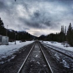 Snow covered railroad track against cloudy sky