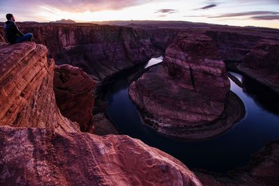 Man sitting and looking at view of rock formation against sky