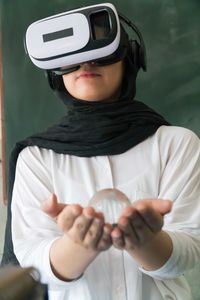 Female student using virtual reality simulator while holding crystal ball in classroom