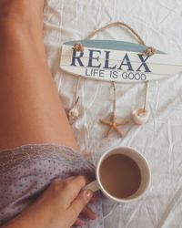 Close-up of woman holding coffee cup on bed