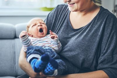 Midsection of woman carrying newborn son yawning on sofa at home